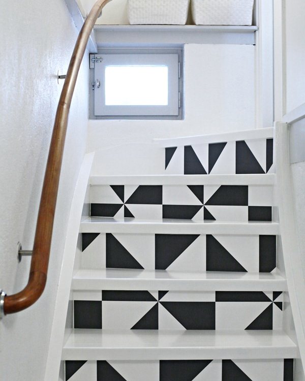 Painted white stairs with grey and white triangle panels on each riser, curved wooden handrail alongside