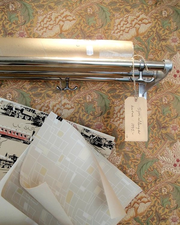 A rolled length of period wallpaper beside a chrome curtain pole