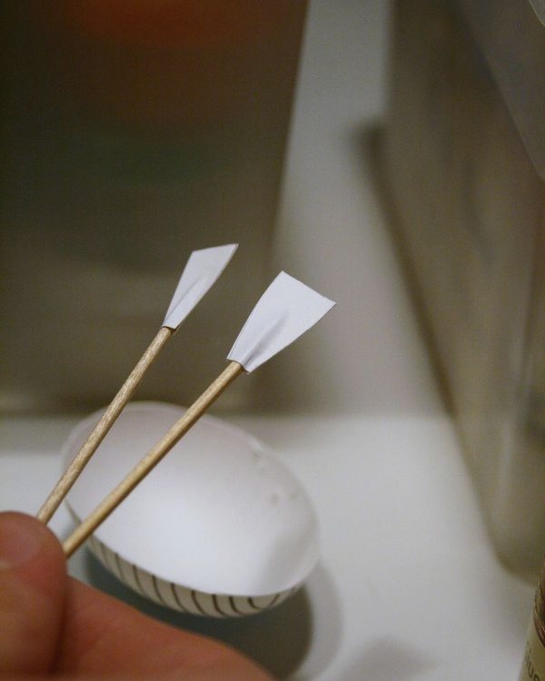A blown egg mounted on a button base with two paper oars made from toothpicks