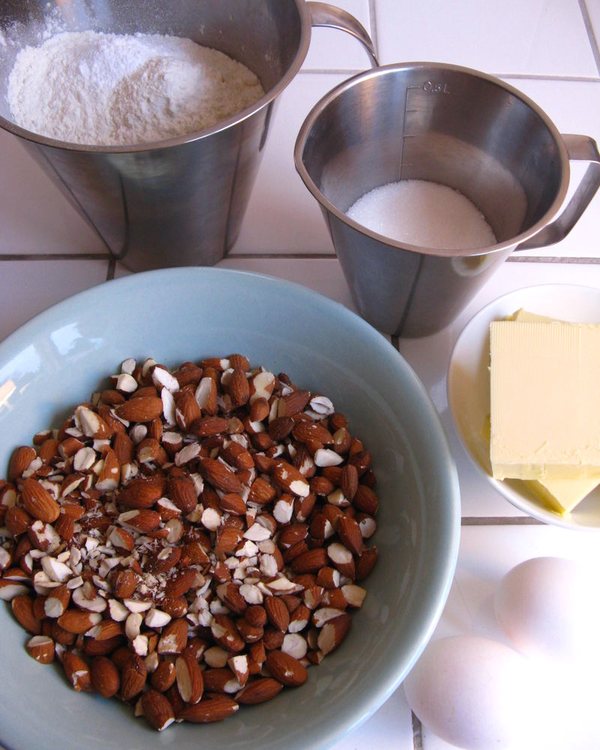 A bowl of roughly chopped almonds beside jugs of flour and milk, butter and eggs