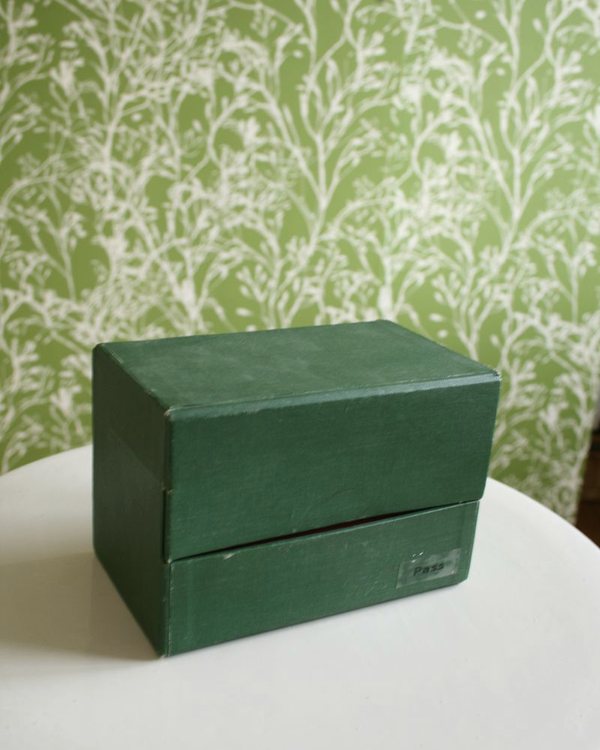 The finished box closed, on a white table against the green wallpaper