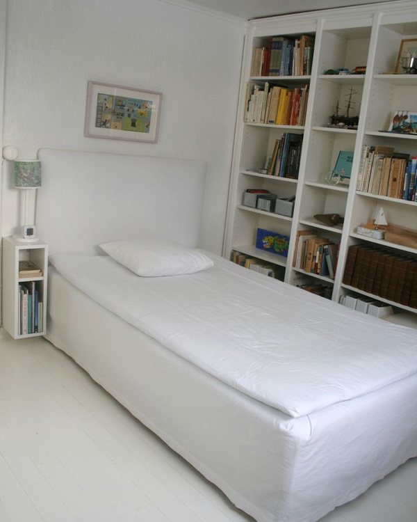 The made bed against a wall of white bookshelves