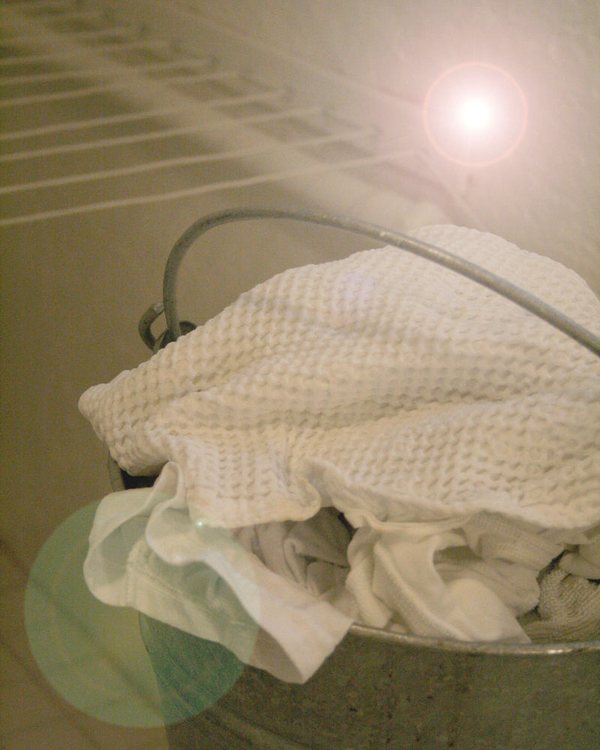 A galvanised bucket of white laundry under a wire shelf