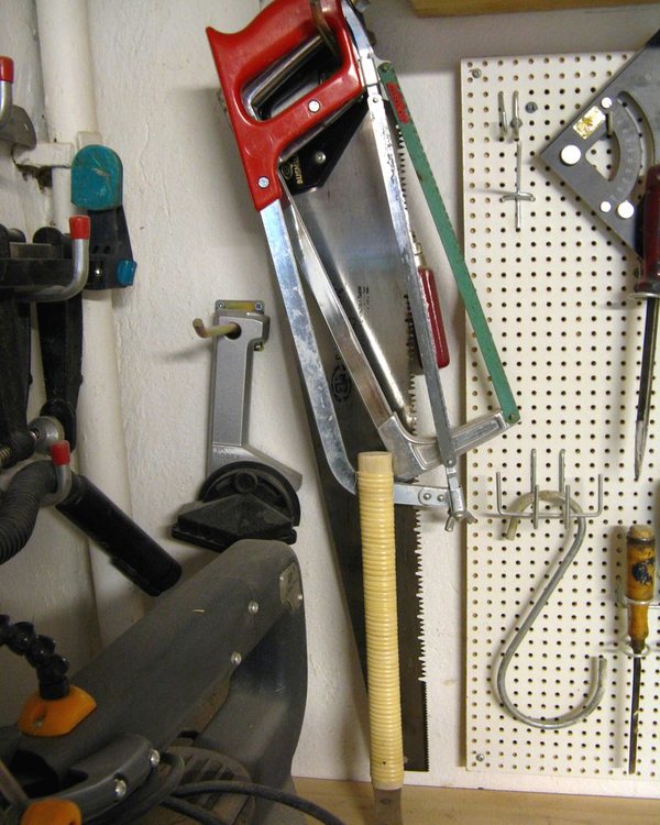 Saws, clamps and a mitre tool hung on pegboard above the bench