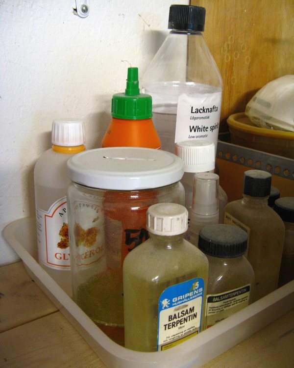 A tray of paint tins, thinners and glues on a garage shelf