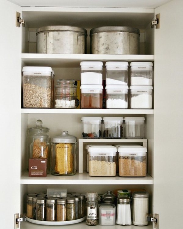 The pantry cupboard open, clear containers on every shelf above a lazy Susan of spices