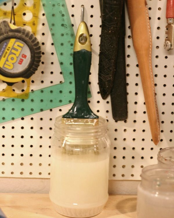 A brush hanging from a hook into a jar of thinner above the workbench