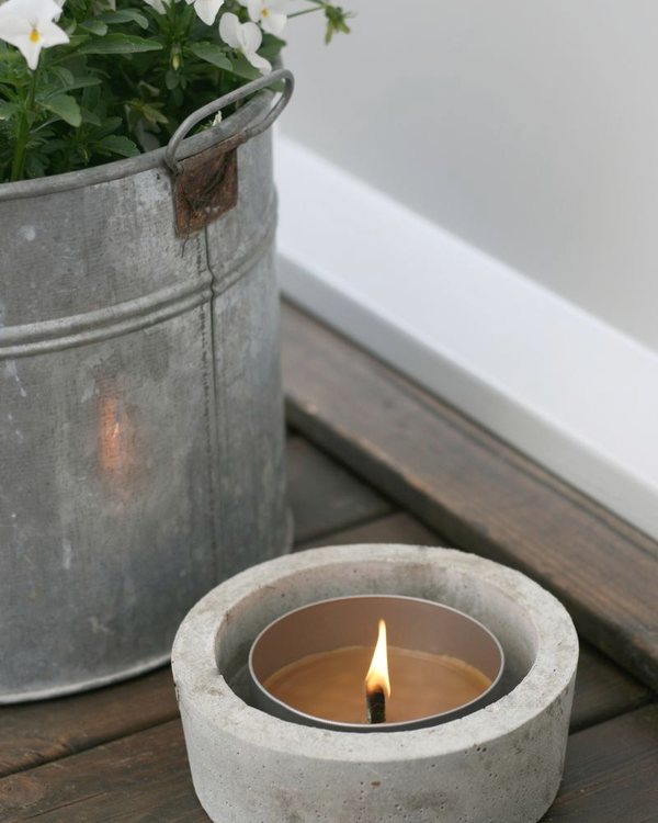 A concrete candle holder on a decked table beside a zinc planter