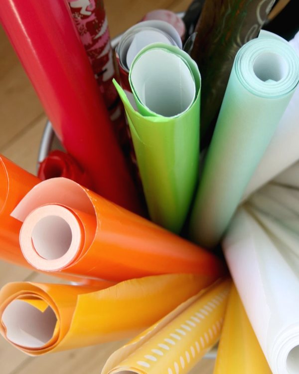 Rolls of wrapping paper standing upright in a bin, seen from above on a wooden floor