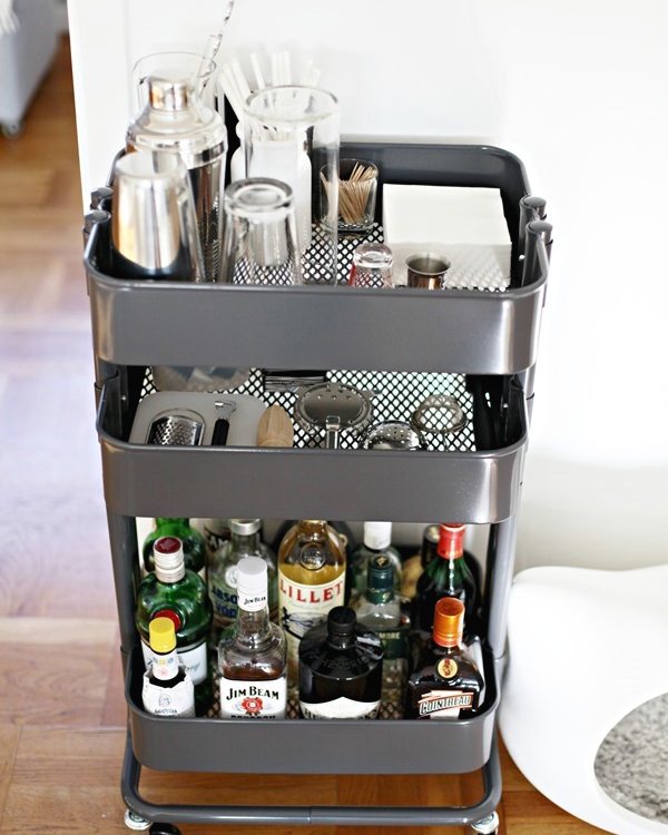 The grey rolling trolley set up as a bar, bottles and glassware on its shelves