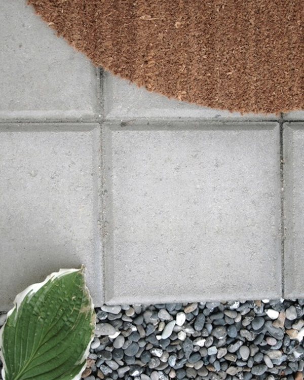The outdoor mat on the gravel, its curved edge against the paving