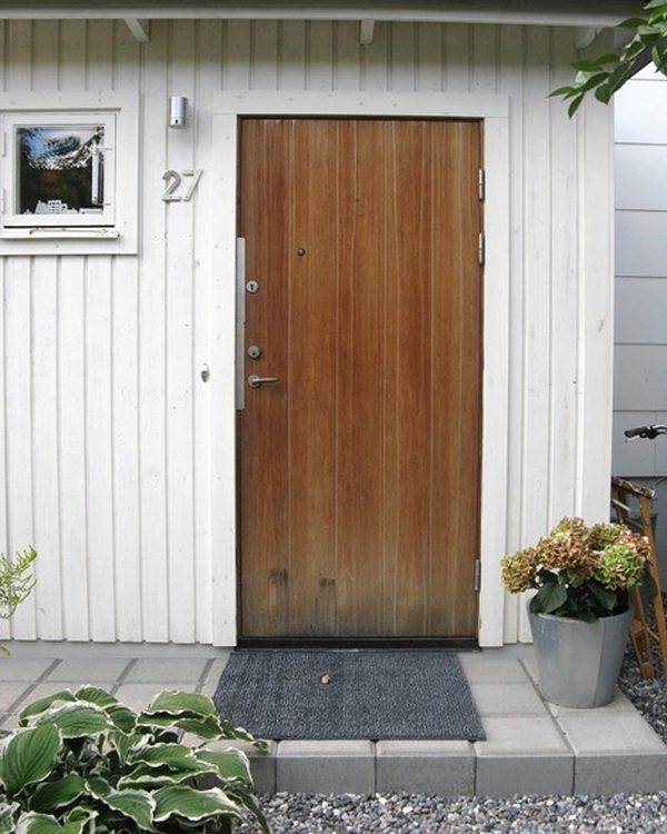 The front door from outside, mat on the step and hostas alongside