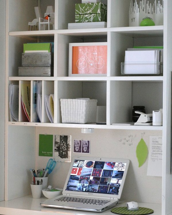 The desk under white cubby shelving, laptop and pinboard