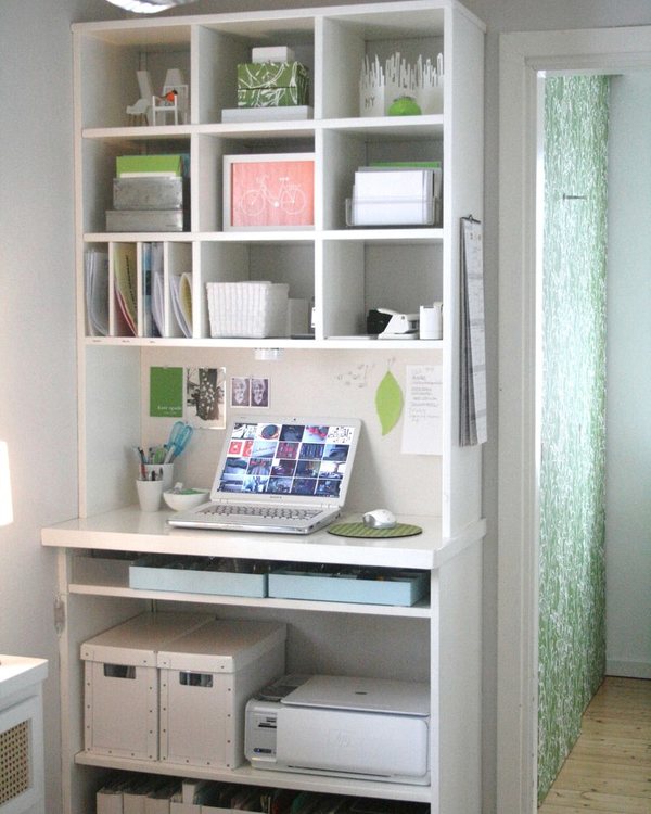 A white shelving unit of open cubbies holding boxes, folders and a printer, beside a doorway